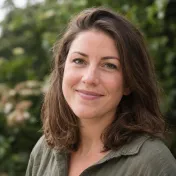 Vrouw met bruin haar en een vriendelijke blik voor een groene achtergrond.
